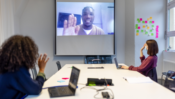 two women sitting in a conference room holding a virtual video meeting with another colleague