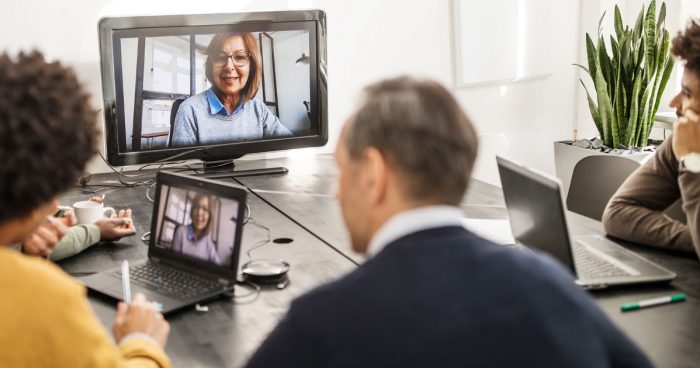 People in an office watching a woman give a presentation on a computer screen