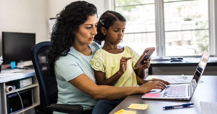 Mother working with young daughter sitting on her lap looking at a phone