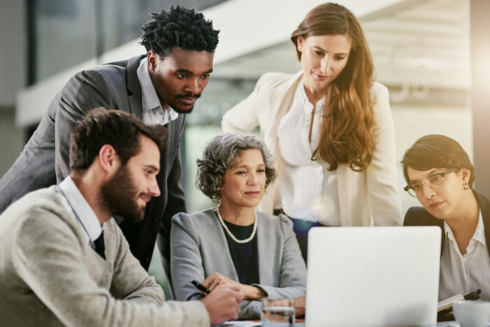 woman leader sitting at computer, surrounded by group of men and women looking at the computer monitor