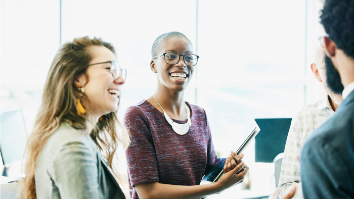 Two business partners or colleagues discussing something and smiling while sitting an a table, facing two colleagues.