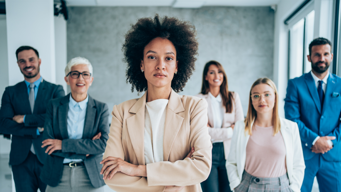 powerful Black woman standing with arms crossed in front of her diverse team in the background