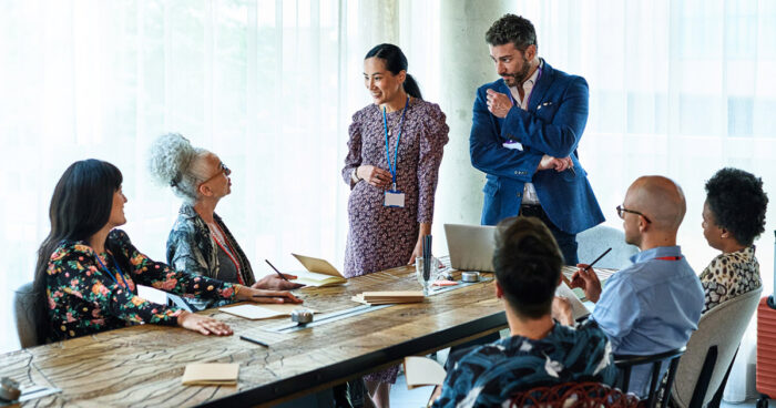 group of business partners or colleagues discussing something and smiling while standing and sitting at a conference table