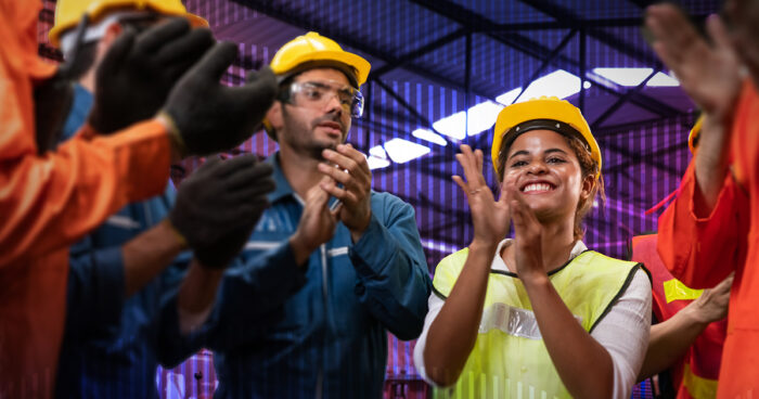 Team of frontline workers wearing hard hats, high-viz vests, and cheering.