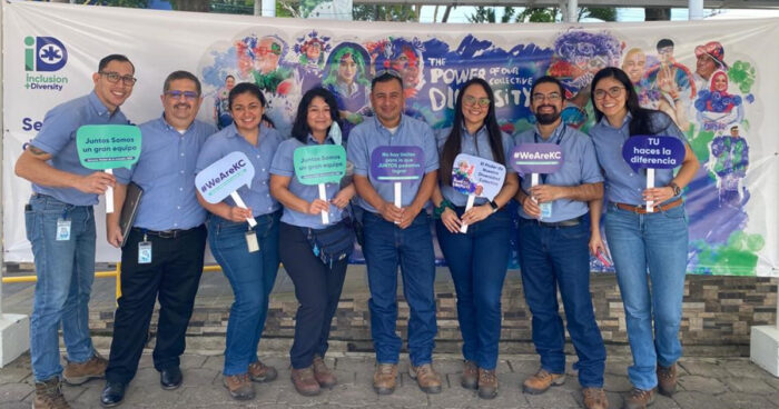 a group of Kimberly-Clark employees standing in front of a mural and holding signs, they are wearing blue shirts and blue jeans.